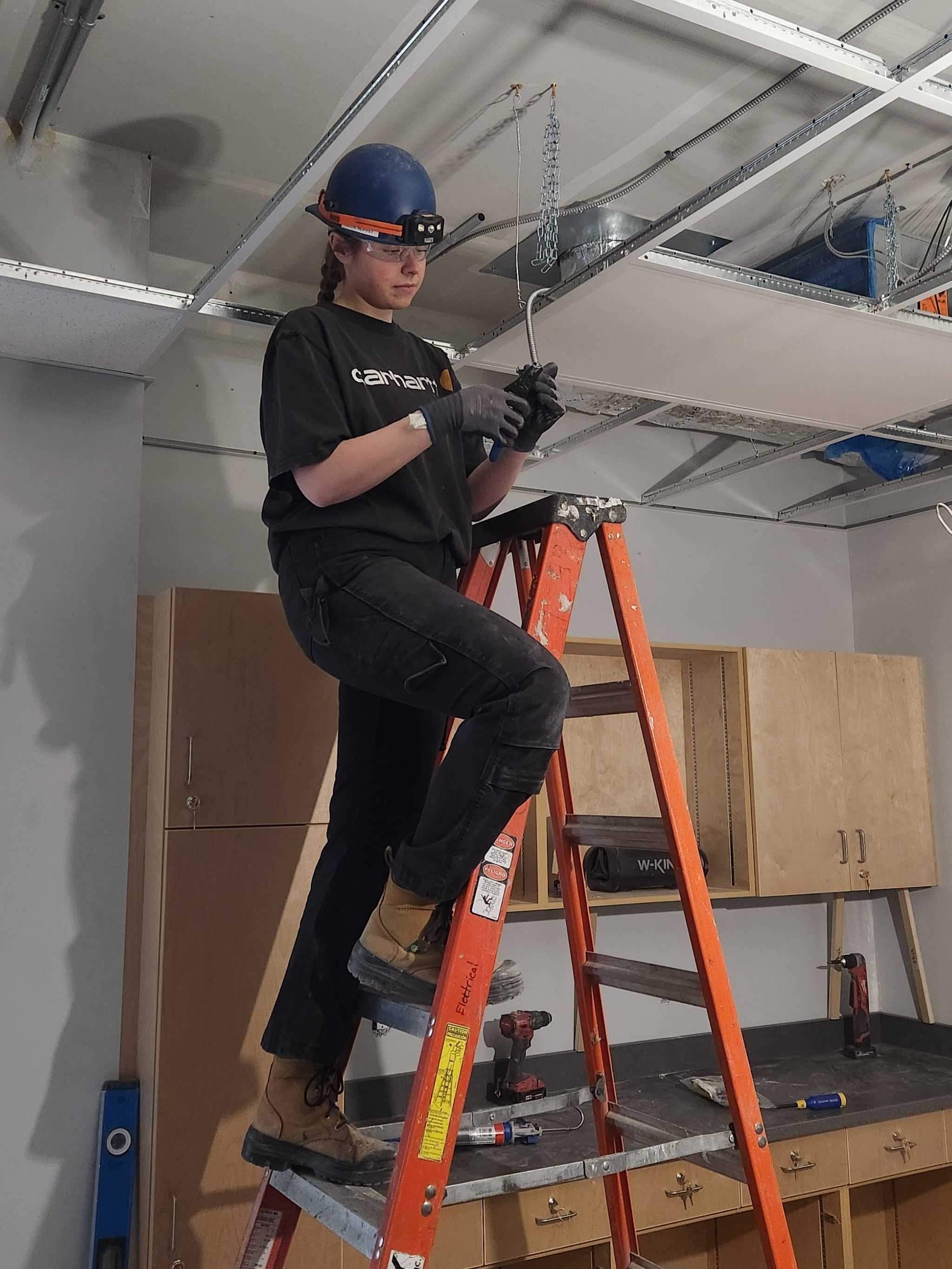Woman with hard hat on ladder doing electrical work